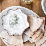 A Bowl of Tzatziki is served with pita bread and photographed from the top view.