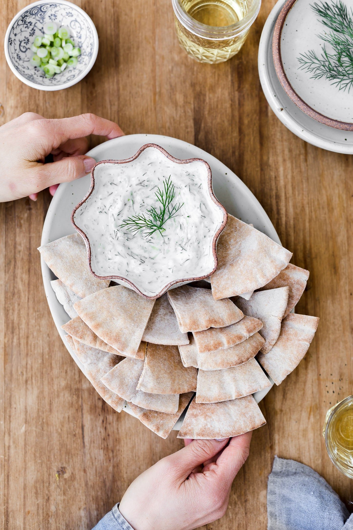 A woman is photographed from the top view as she is serving tzatziki sauce with pita bread.