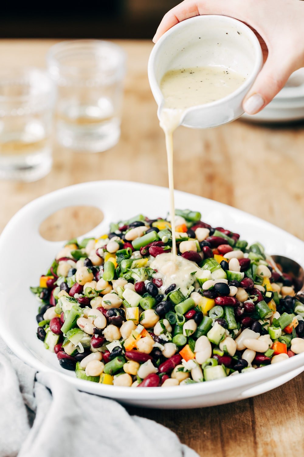 A woman is pouring salad dressing on a bowl of five bean salad photographed from the front view.