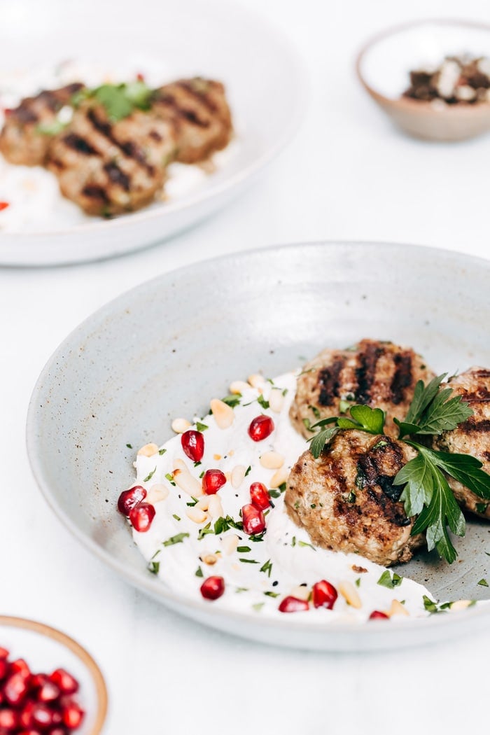A plate full of yogurt tahini sauce and Turkish meatballs are photographed from the front view.