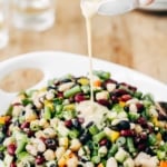 A bowl of Five Bean Salad is being drizzled with dressing photographed from the front view.