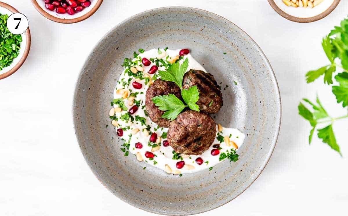 Turkish meatballs placed on a bed of tahini yogurt sauce and garnished with pine nuts and pomegranate.