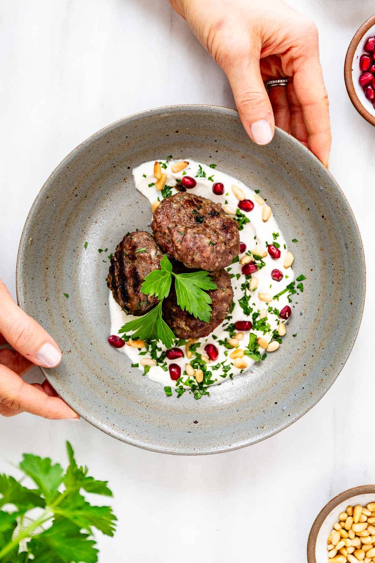 A bowl spread with yogurt tahini sauce and Turkish meatballs garnished with pomegranate seeds and pine nuts.