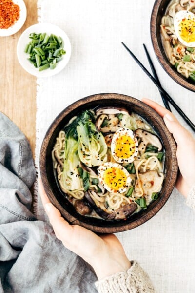 A woman is photographed from the top view as she is serving a bowl of Weeknight Vegetarian Ramen Bowl with Shiitake Mushrooms and Bok Choy