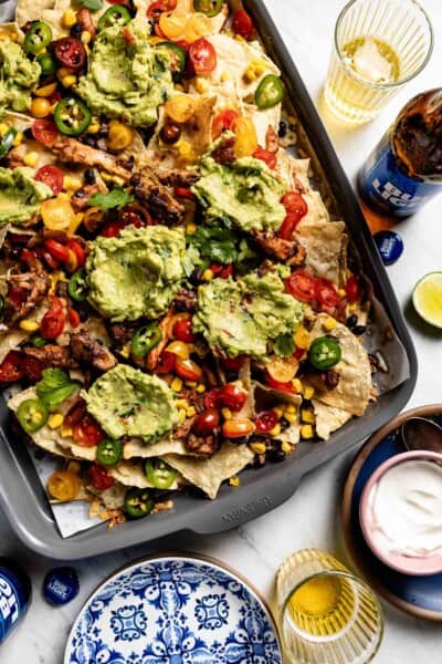 Shredded chicken nachos on a sheet pan topped of with guacamole.