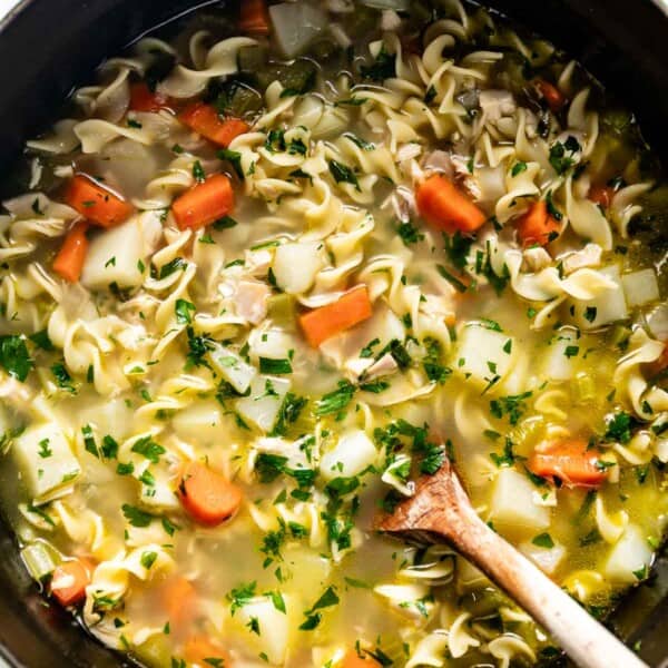 Chicken noodle soup with potatoes in a big pot with a wooden spoon on the side.
