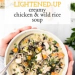 A bowl of Lightened-Up Creamy Chicken and Wild Rice Soup is in the hands of a woman photographed from the top view.