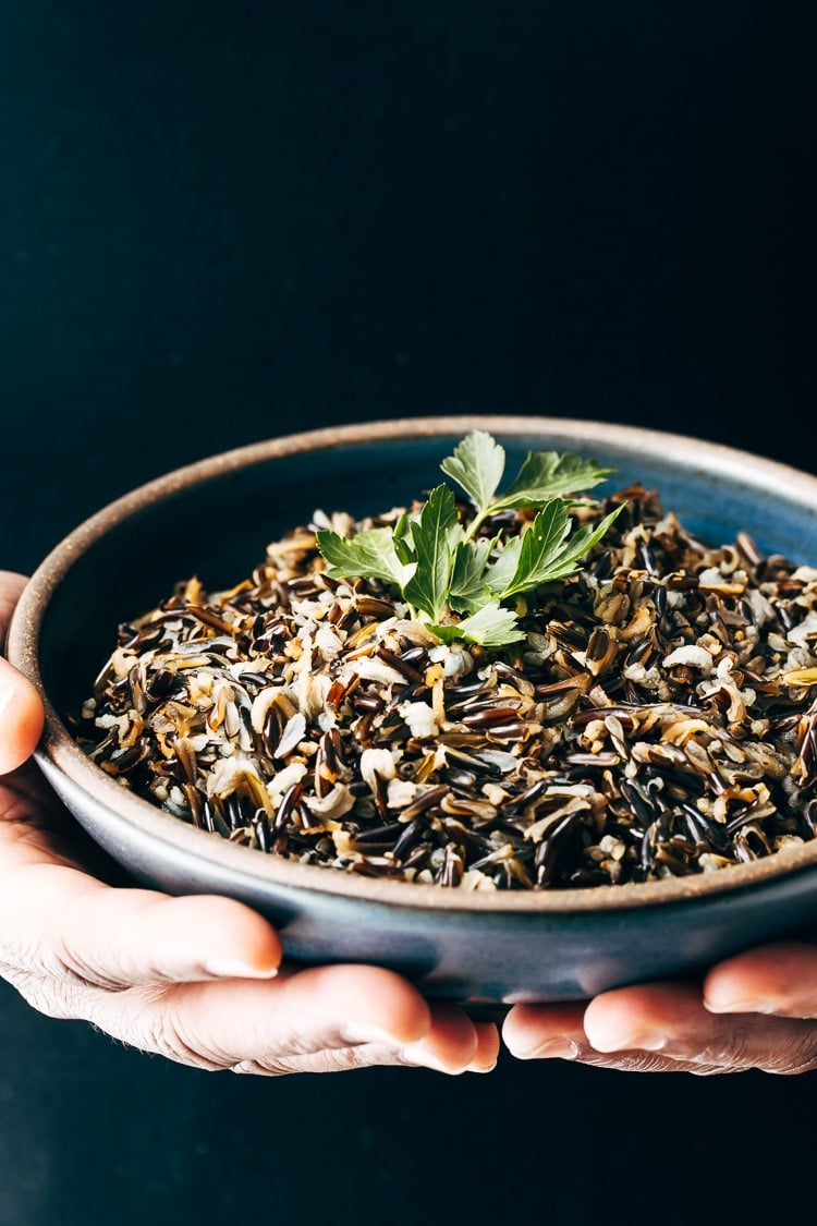 A man is photographed from the front view (close up) with a bowl of cooked wild rice garnished with a few leaves of parsley for the How To Make Wild Rice Recipe post.