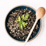 A bowl of cooked wild rice garnished with fresh parsley is photographed from the front view for the how to cook wild rice recipe post