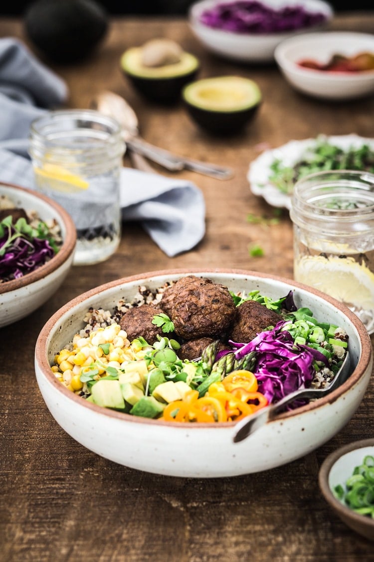 A bowl of quinoa power bowl topped off with colorful veggies is photographed from the front view.