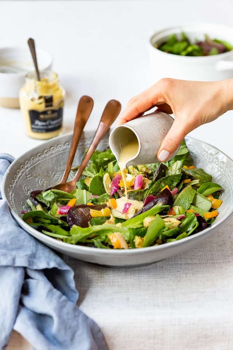 a woman is drizzling a salad with her Lemon Dijon Vinaigrette Recipe