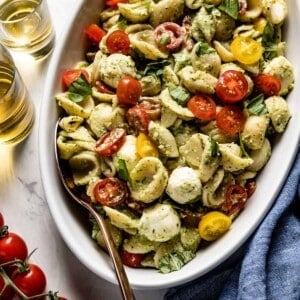 pesto caprese pasta salad in a salad plate with a spoon on the side