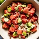 Watermelon and cucumber salad in a bowl with two spoons in the bowl.