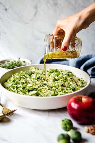 Chopped Brussel Sprouts are being drizzled with the salad vinaigrette.