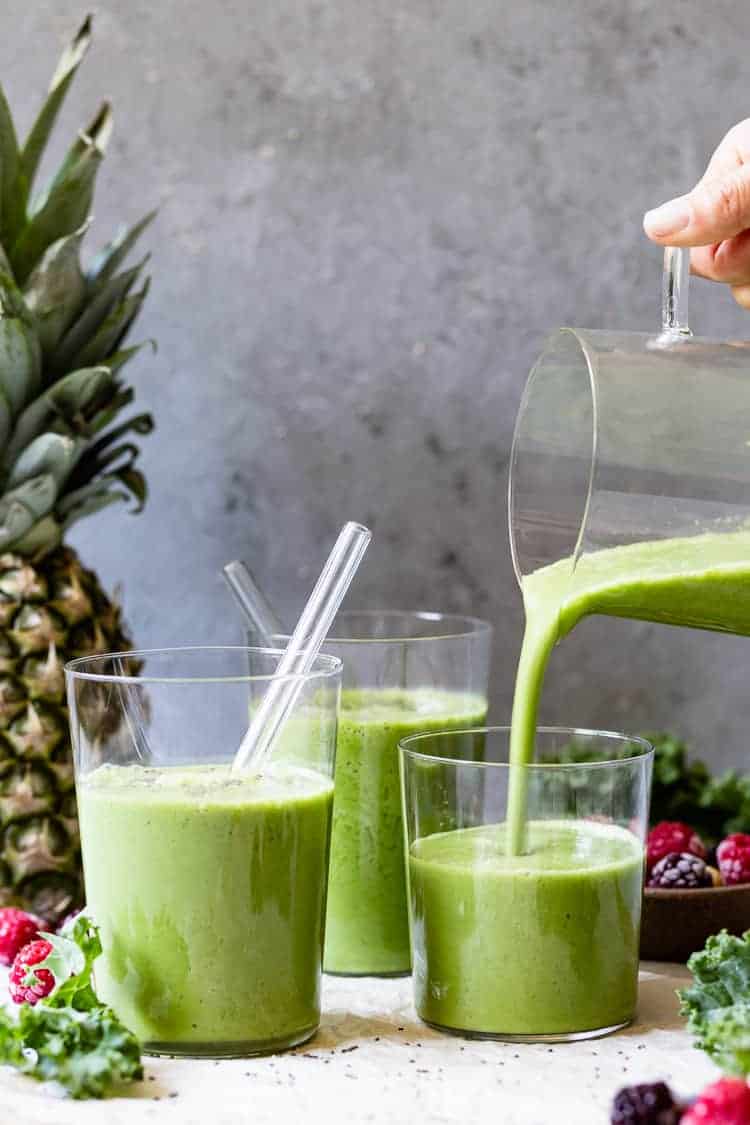 A woman is pouring green smoothie into a glass.