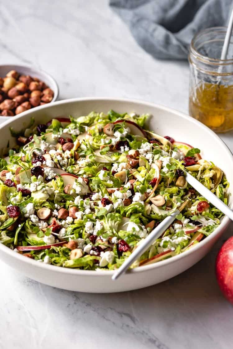 Shaved Brussel Sprout Salad Recipe served in a bowl with utensils in the bowl.