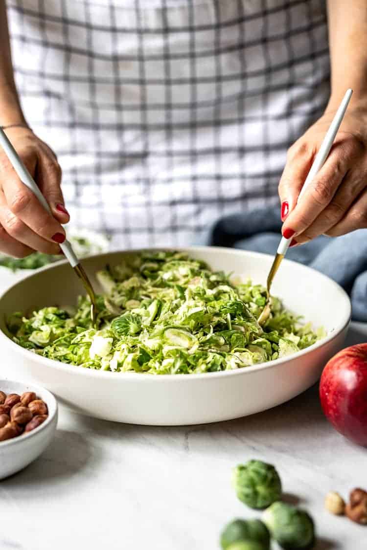 How do you shave brussel sprouts - A woman is photographed as she is mixing raw brussels sprouts salad.