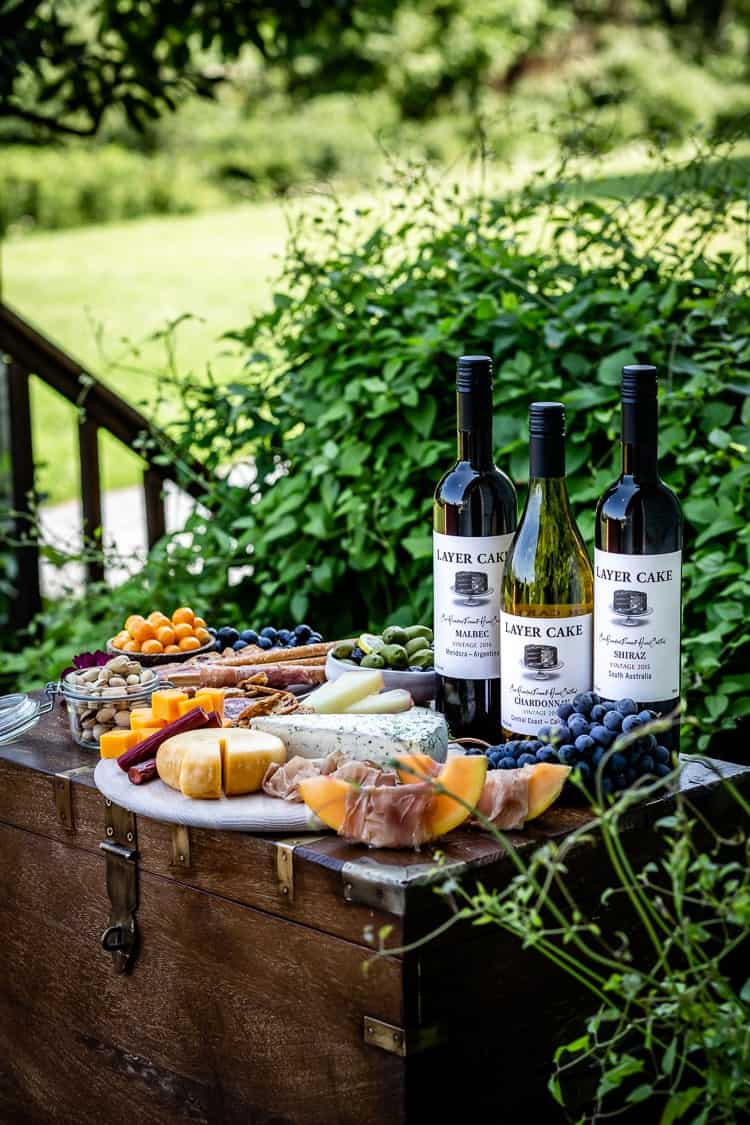Bottles of wine with cheese, meat and fruit in a garden. Learn all my tips and tricks on how to put together the best meat and cheese platter for all your entertaining needs. 