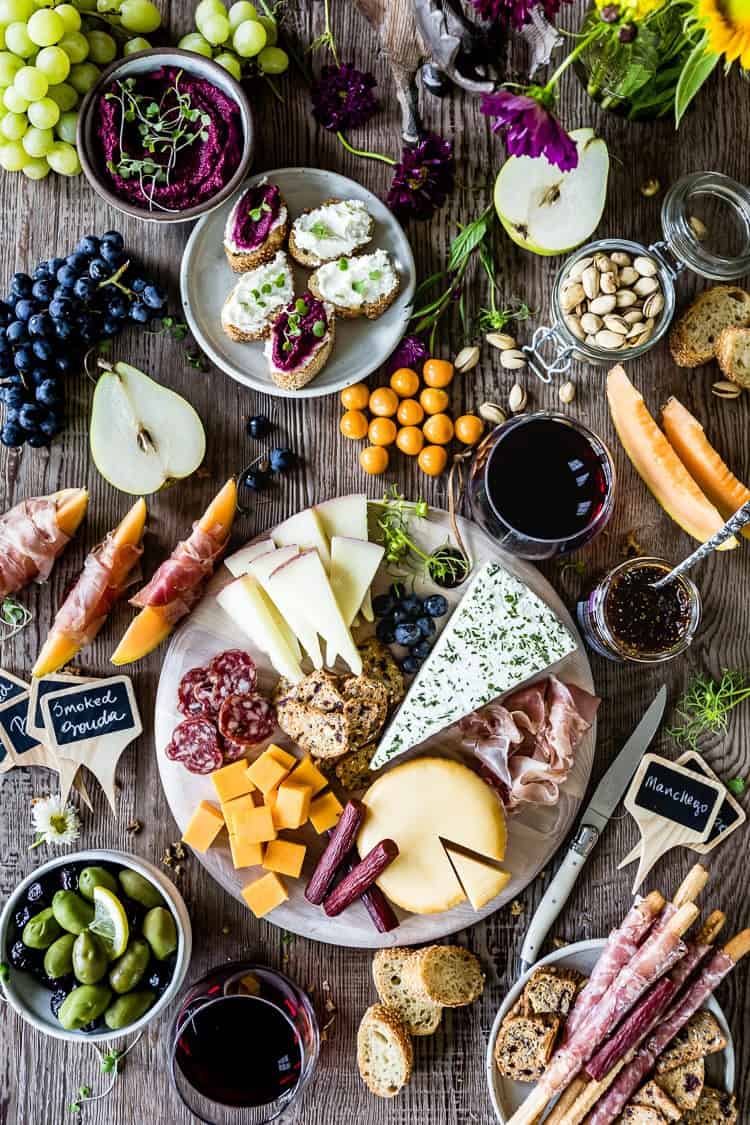 cheese board ideas with various cheeses, meats, olives, wine and bread