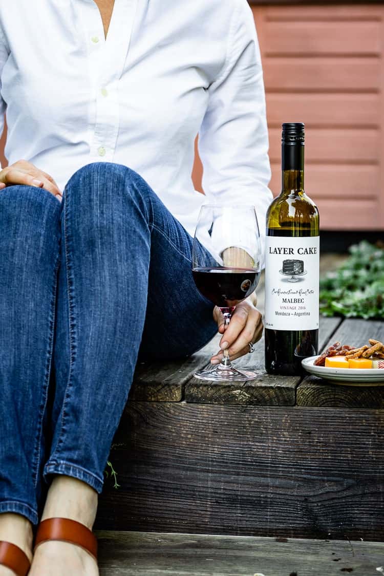 A woman is holding a glass of wine with a bottle next to it with a plate filled with Cheese and Meat