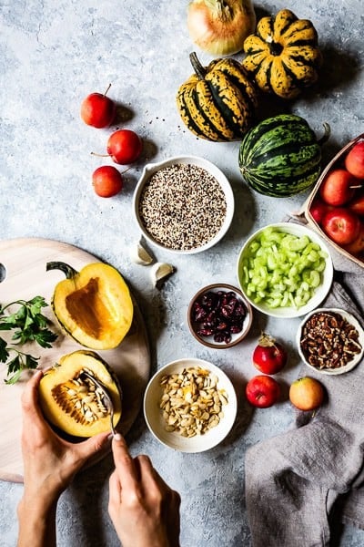 Ingredients for Roasted acorn squash with quinoa - a woman is scooping the seeds of an acorn squash