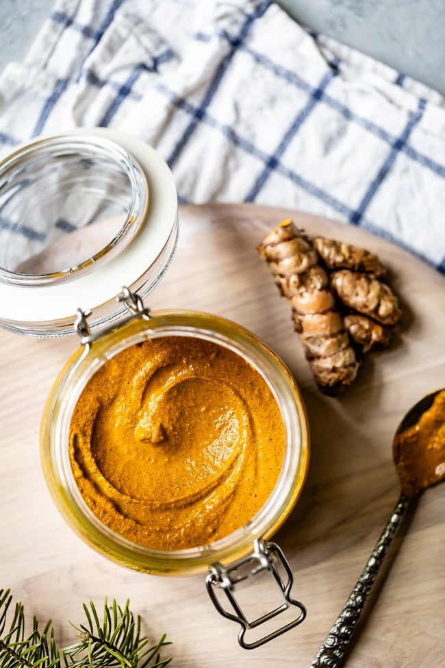 A photo of turmeric paste photographed in a jar with fresh turmeric root on the side