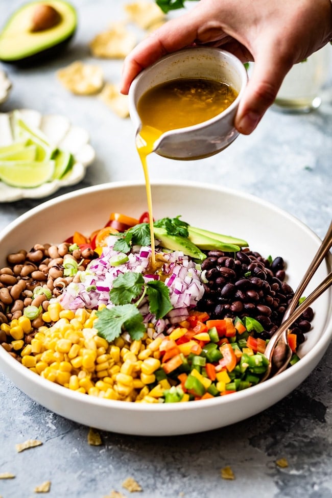 Easy Mexican caviar is photographed from the front as a woman is drizzling it with dressing