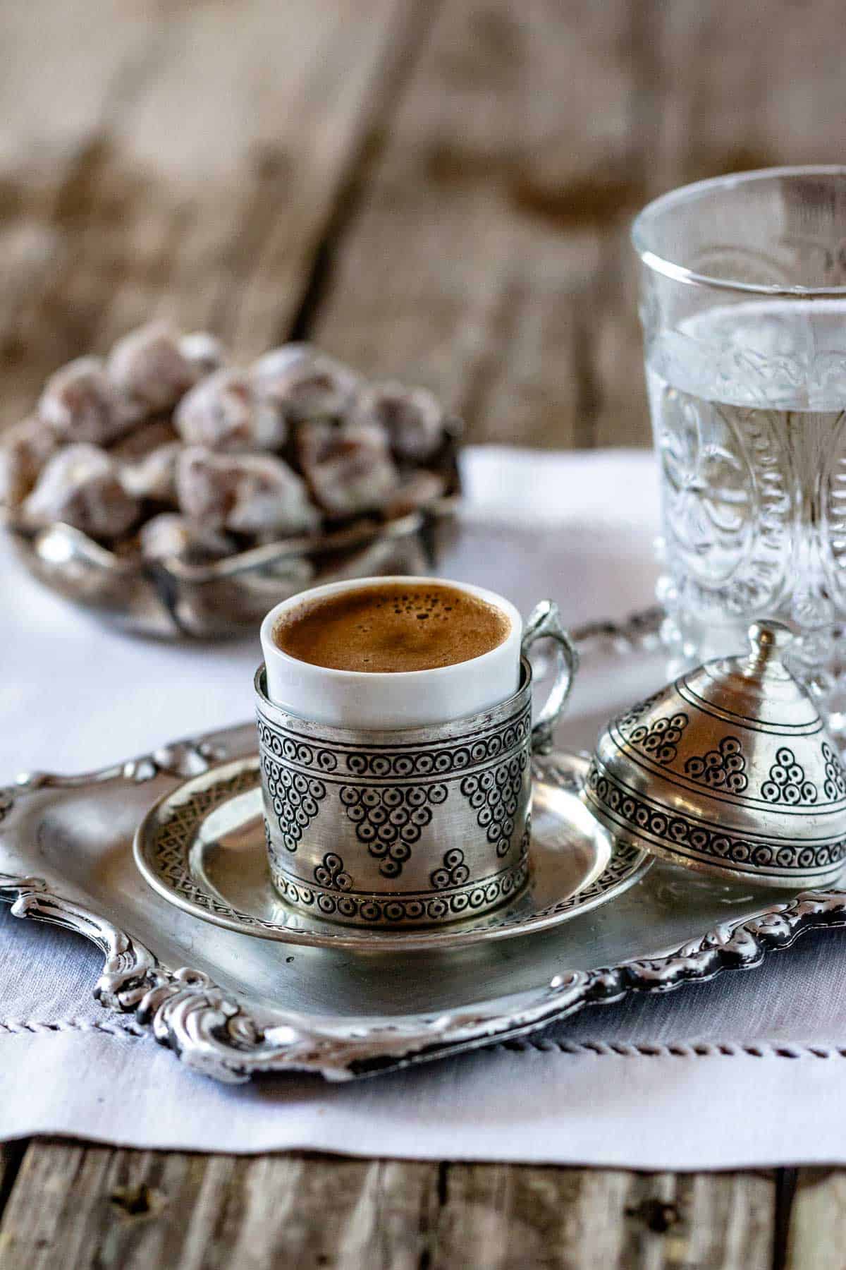 Traditional Turkish coffee served in a silver zarf cup on a tray with Turkish delight and a glass of water.