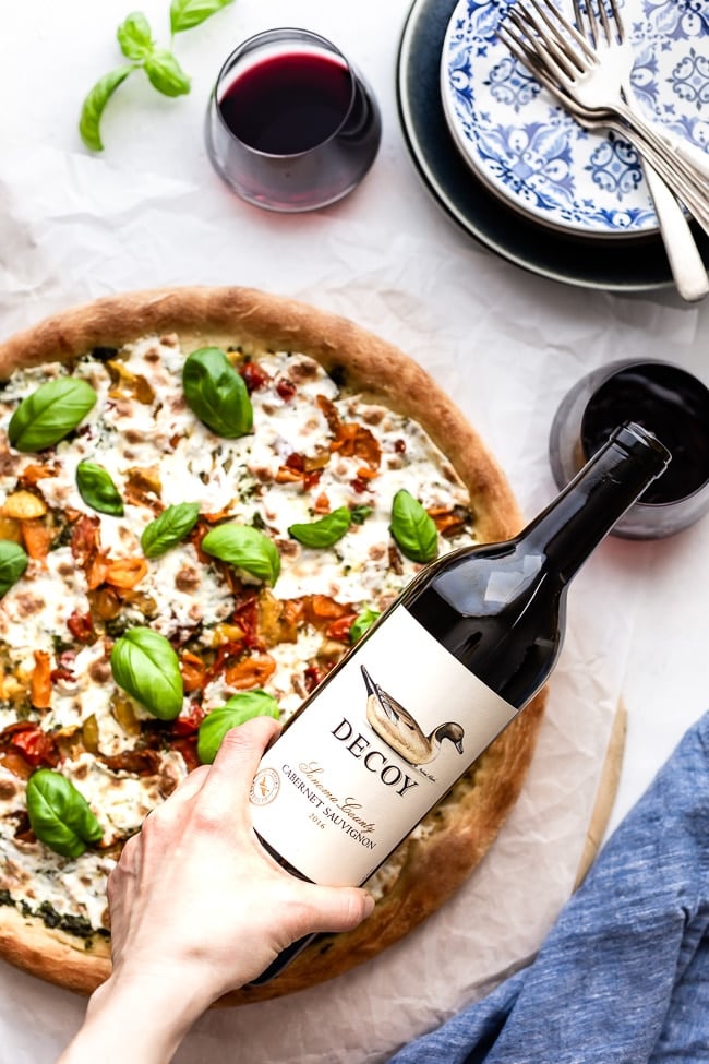 This delicious Homemade Caprese Pizza is filled with mozzarella, tomato, and basil is being served with a bottle of wine.