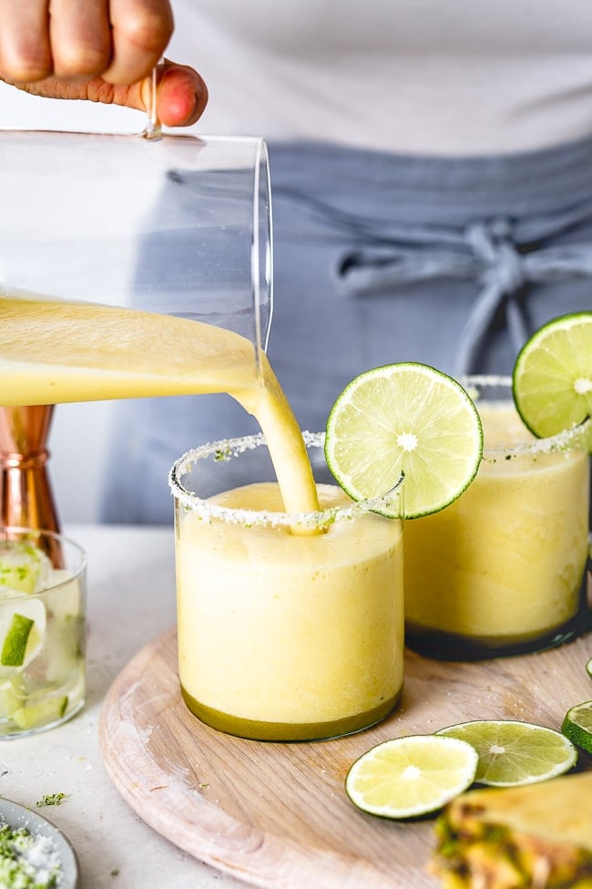 person pouring in pineapple margarita in a glass.