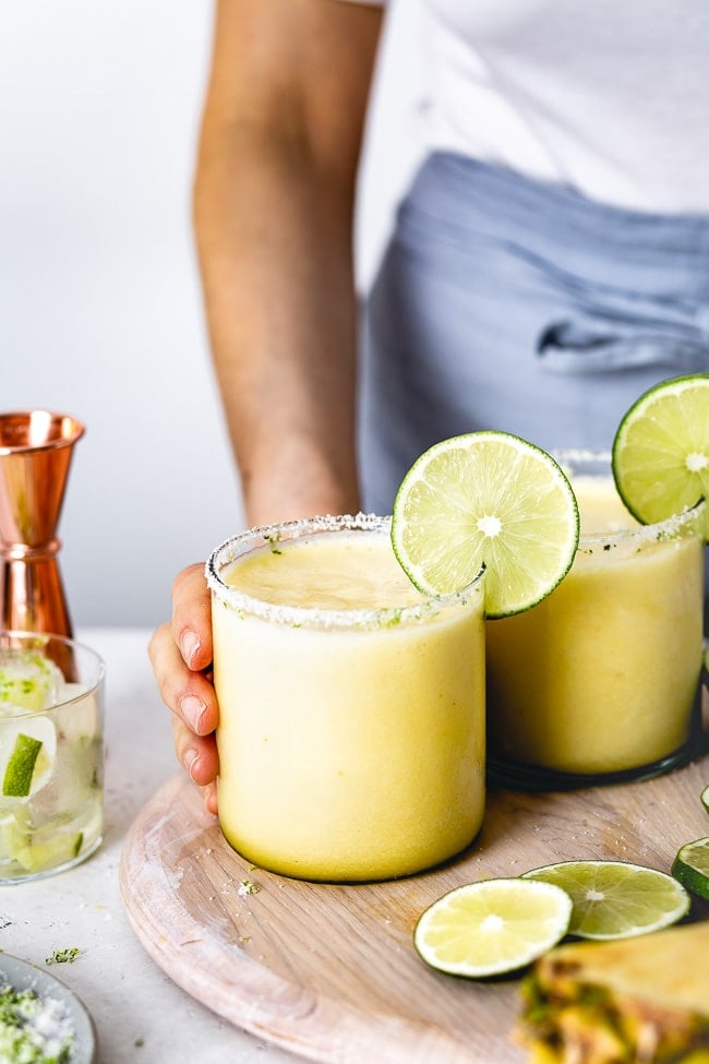 frozen pineapple margarita recipe garnished with a slice of lime is being served by a woman photographed from the front view.