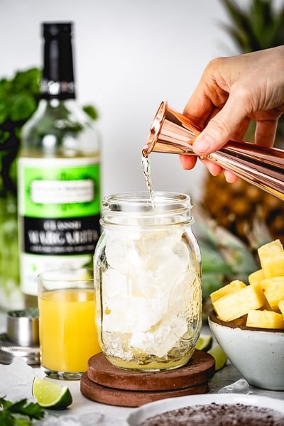 A woman is pouring tequila into a mason jar to make this drink