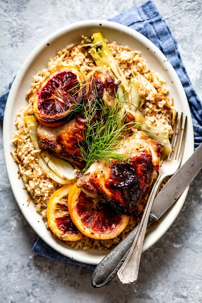 A plate filled with roasted chicken with fennel on a bed of bulgur pilaf and garnished with fennel fronds on top.