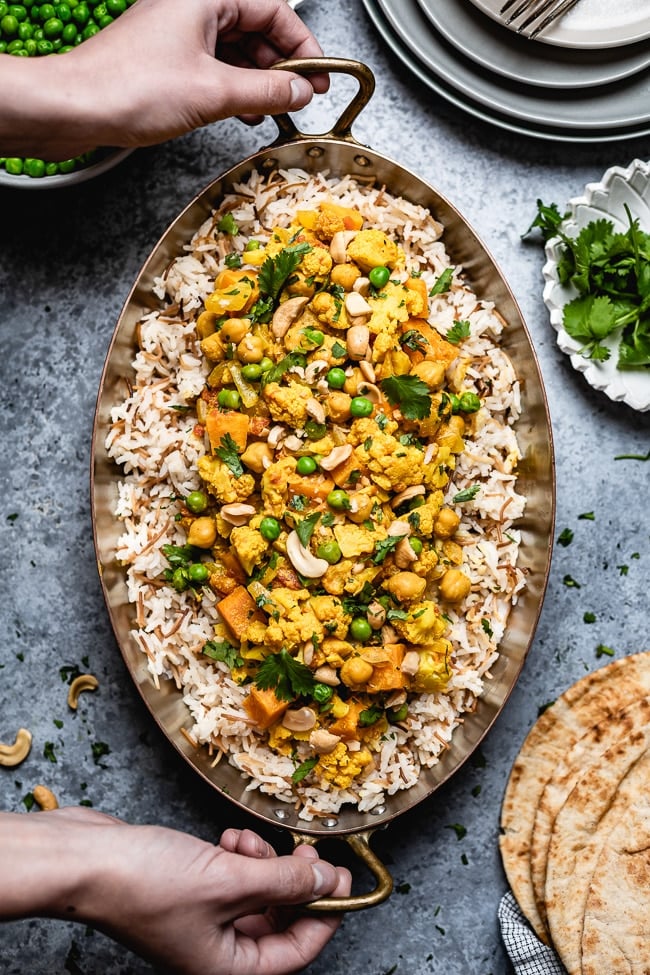 Indian Style cauliflower curry spread over rice and photographed from the top view as a woman is placing it on the table.