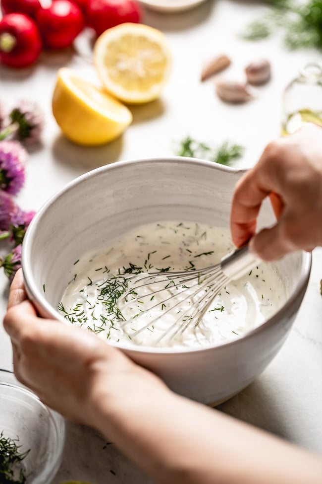 A woman is photographed as she is whisking a bowl of creamy healthy yogurt dressing.