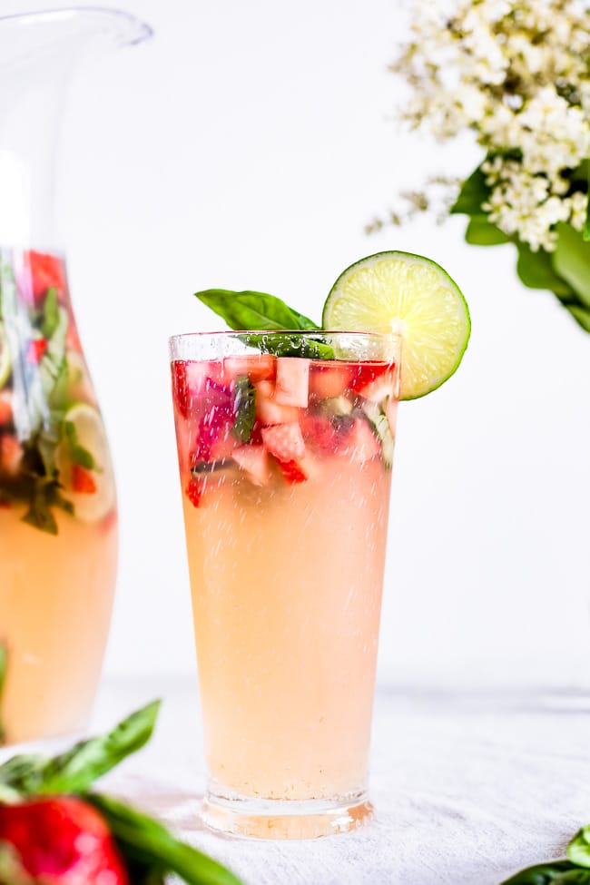 A glass of Strawberry basil limeade is garnished with a slice of lime and photographed from the front view.