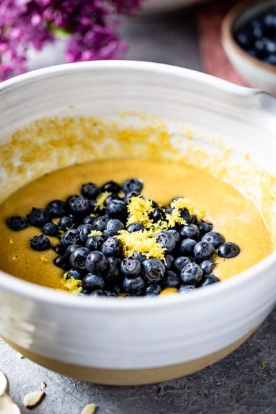 the batter for this recipe is topped off with fresh blueberries and lemon zest