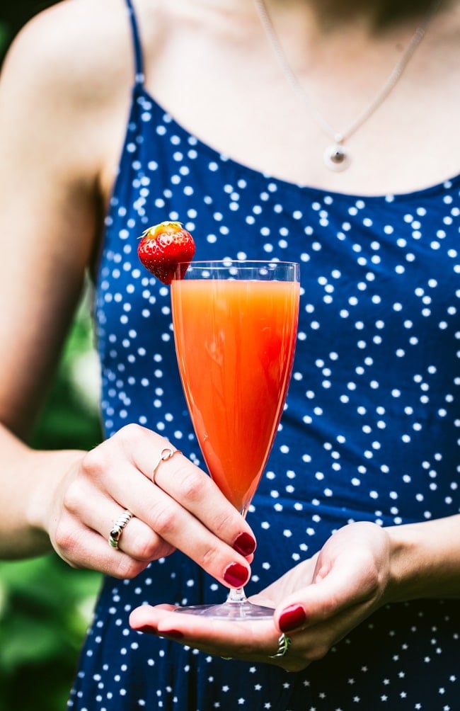 Blood Orange Mimosa garnished with a strawberry photographed in a woman's hand.