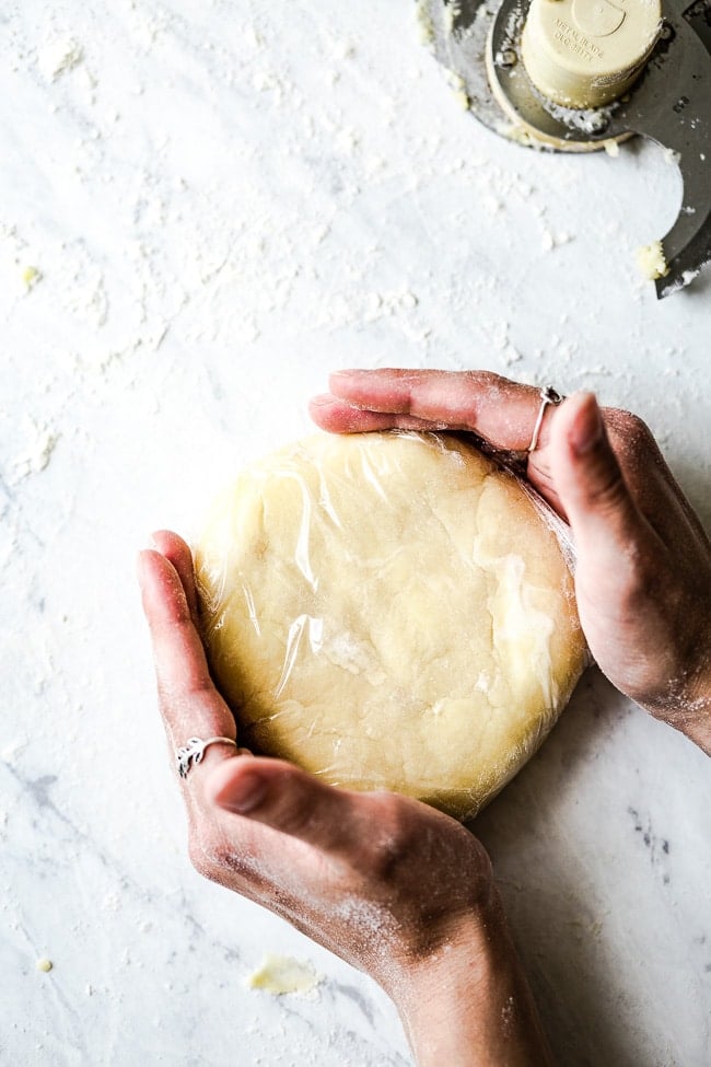 homemade galette dough turned into a disk wrapped in stretch film photographed from the top view.