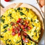 Overhead view of spinach and feta egg bake sliced on a wooden board and topped with tomatoes.