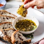 Bread dipped in olive oil dipping sauce in a person's hand.
