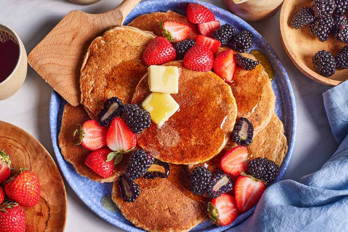 Pancakes made with almond flour on a plate topped off with maple syrup and berries.