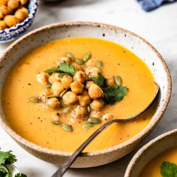 Vegan sweet potato soup garnished with chickpeas with a spoon in the bowl