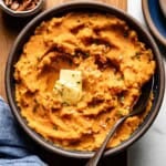 Mashed sweet potatoes in a bowl garnished with butter and thyme.