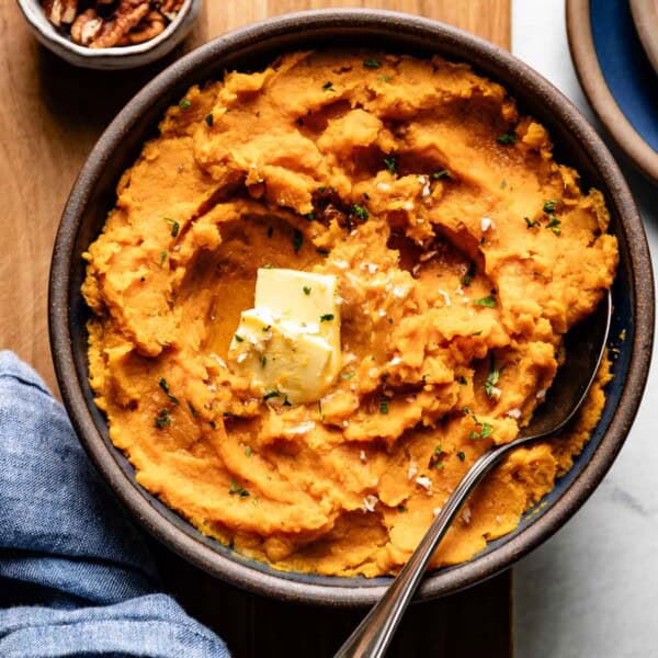 Mashed sweet potatoes in a bowl with butter and thyme on top.