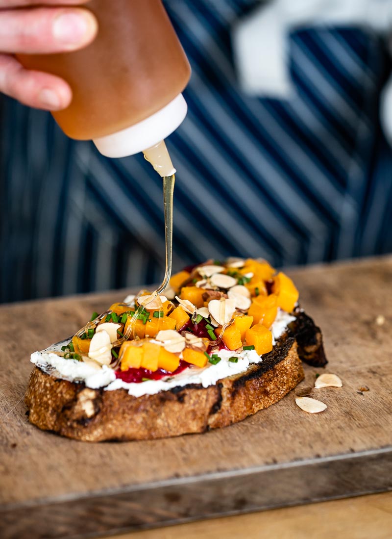 Goat cheese bruschetta with roasted butternut squash is being drizzled with honey