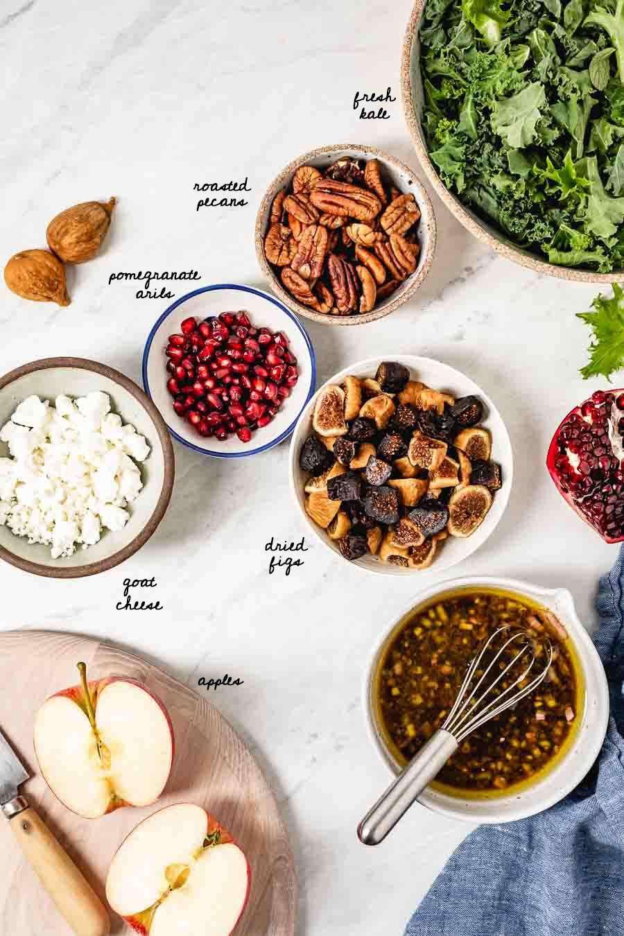 Harvest Kale Salad Ingredients: Kale, pecans. pomegranate arils, goat cheese, figs, and apples are photographed from the top view.