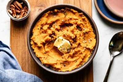 Mashed sweet potatoes in a bowl garnished with butter, thyme, and pecans.