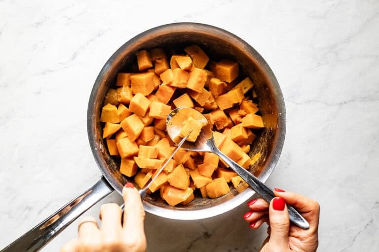 Person checking the doneness of a sweet potato cube with a knife.