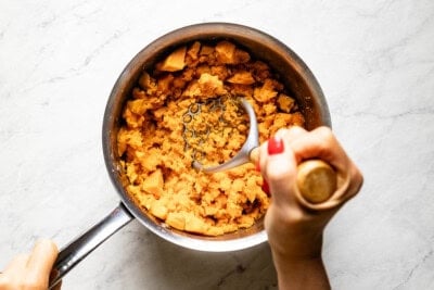 Person mashing sweet potatoes with a potato masher.